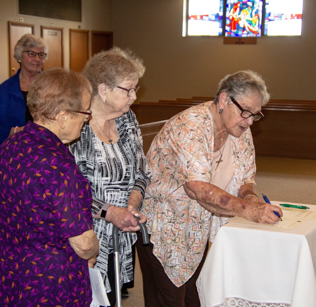 Three religious sisters sign a document on a small table