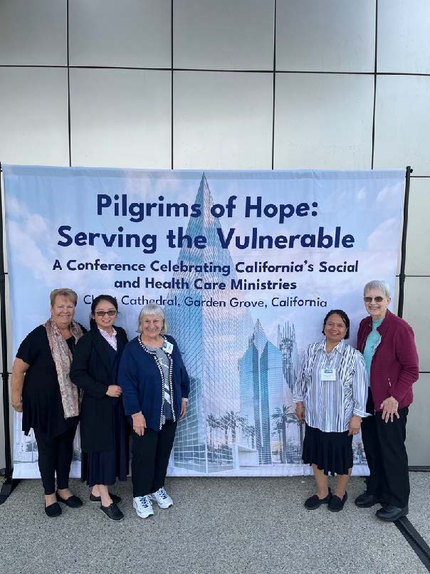 A group of religious sisters poses in front of a conference banner.