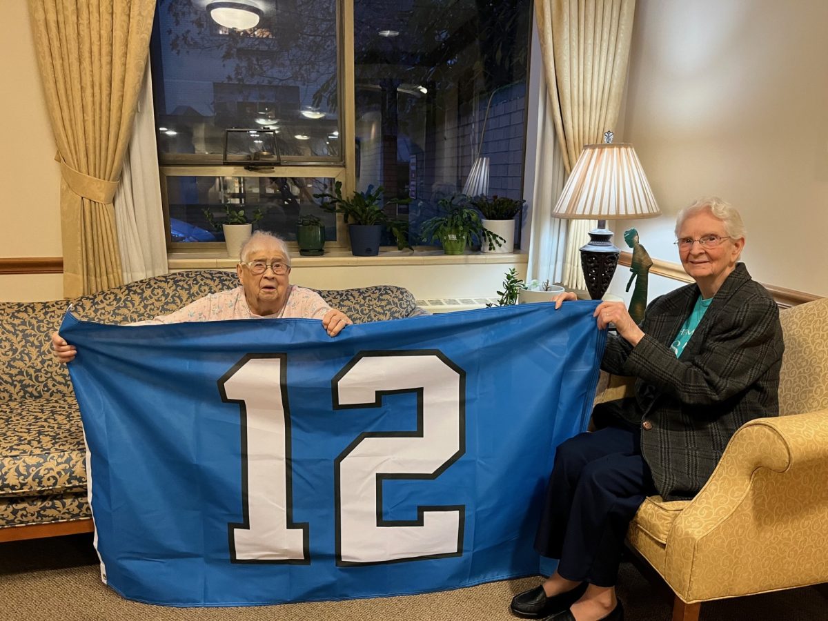 Two religious sisters pose with a flag with a 12 on its center, also known as the emblem for the Seattle Seahawks fan base.