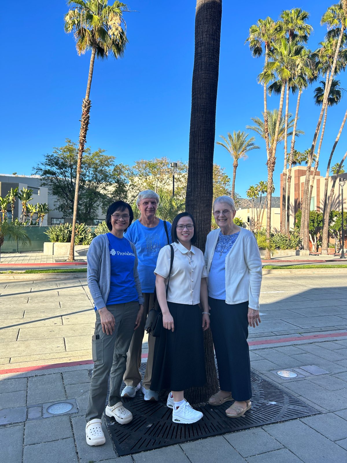 Four members of the Providence SoCal Community pose for a picture in front of palm trees.