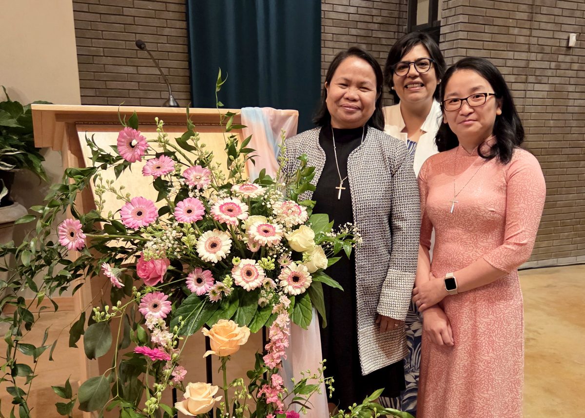 Three Sisters of Providence pose for a group portrait next to a flower-adorned podium.